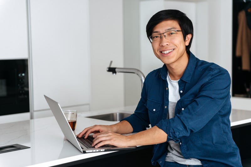 Smiling asian man working on laptop computer remote support